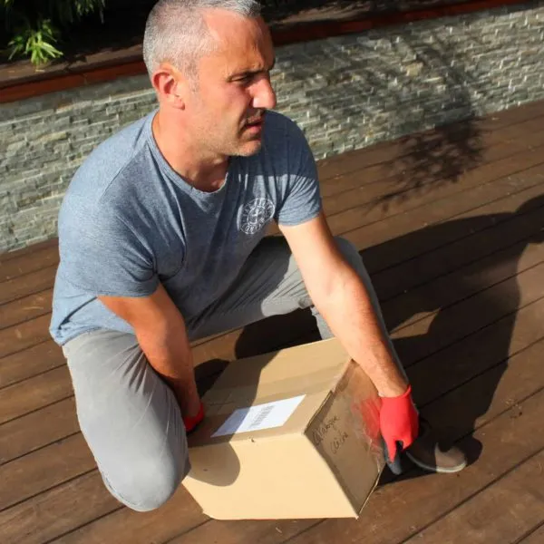 Homme soulevant une boîte avec des gants rouges.